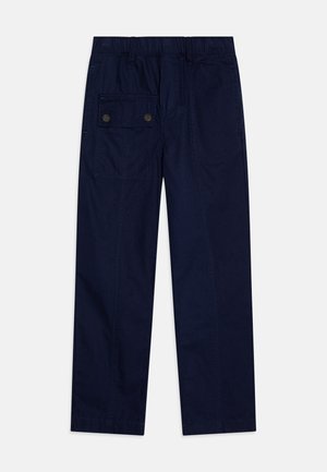 Sötétkék pamut nadrág, rugalmas derékrésszel, egyenes lábformával, és egy nagy oldalzsebbel, amelyen két gomb található.