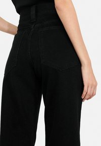 Jeans in denim nero a vita alta con tasche posteriori, una finitura pulita e un tessuto testurizzato. La vestibilità è dritta e spaziosa.