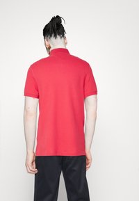 Polo shirt rosso a maniche corte con colletto, realizzato in tessuto liscio. Presenta un design pulito e semplice e un orlo dritto.