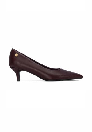 Zapato de salón de cuero marrón oscuro con punta afilada, tacón bajo y un pequeño logo circular dorado cerca del talón en el lado exterior.