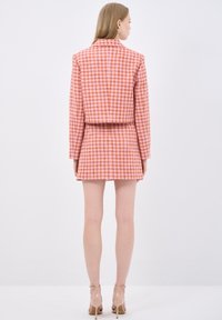Różowa i pomarańczowa marynarka i spódnica w wzór pied-de-poule, charakteryzująca się strukturalnym fasonem, krótką kurtką i rozkloszowaną spódnicą. Przezroczyste obcasy.