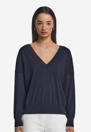Maglione blu navy a V con maniche lunghe, texture morbida, vestibilità rilassata e orlo a costine. Design semplice, senza motivi o decorazioni.