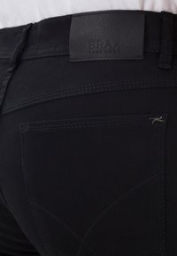 Black denim jeans with a smooth texture, featuring a leather waistband label, subtle stitching details, and a back pocket design.