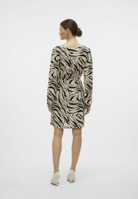 Beige jurk met lange mouwen en zwarte zebra-stripes, met een ceintuur in de taille, op knielengte, met een soepele textuur, gecombineerd met lichtgekleurde hakken.