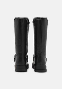 Bottes hautes jusqu'au genou en cuir noir à finition lisse, avec des fermetures éclair latérales et une semelle en caoutchouc texturée. Comprend des détails accentués courbes sur le talon.