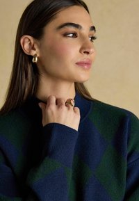 Tume ja roheline argyle muster, ribiga krae, kuldsed pirnikujulised kõrvarõngad ja kuldne sõrmus ainulaadse põimimismustriga. Sile tekstuur.