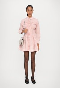 Dress in denim rosa con colletto, due tasche sul petto e gonna a pieghe. Abbinato a ballerine nere a pois e a una piccola borsa a tracolla beige.