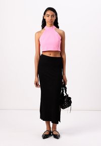 Roza halter crop top v kombinaciji s črno rebrasto maxi krilo z bočnim razporkom. Dopolnjeno s črno torbico in ravnimi čevlji z okraski.