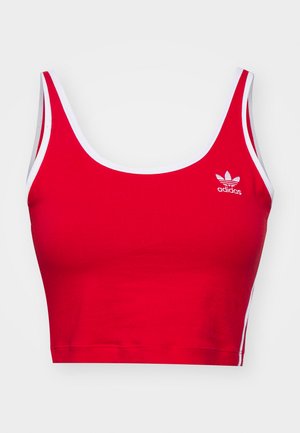 Červený crop top vyrobený ze strečového materiálu, s kulatým výstřihem, širokými ramínky, bílými akcenty a vyšitým logem Adidas na hrudi.