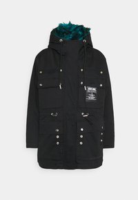 Svart parka-jacka med dragkedjefickor, dragsko och ett teal-färgat fuskpälsfoder i huvan. Har detaljer med knappar och kardborre.