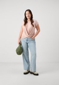 Ανοιχτό ροζ μπλουζάκι με κόμπο, ανοιχτό μπλε παντελόνι φαρδύς γραμμής, κρεμ παπούτσια και πράσινη φουσκωτή τσάντα. Απλός σχεδιασμός, casual εφαρμογή και μαλακή υφή.