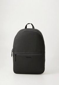 Black backpack made of smooth fabric, featuring a rounded shape, top handle, and front zip pocket. Subtle engraved logo on the body.