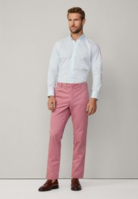 Camisa de botones azul claro, de tela ligera, de manga larga; pantalones rosas, de mezcla de algodón, corte recto, con zapatos de cuero marrón.