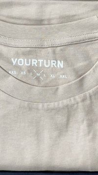 Beežist puuvillast T-särk, millel on valgete tähtedega bränd "YOURTURN", kaela all on trükitud suuruse indikaatorid XXS kuni XXL.