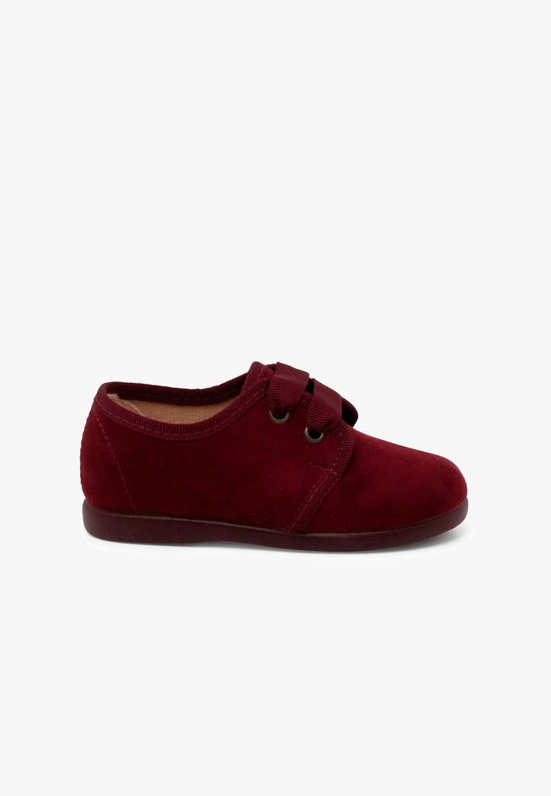 Chaussure en daim rouge avec un bout arrondi, fermeture par sangle élastique et semelle plate. Texture lisse avec un design simple et des accents de couture.