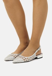 Des chaussures à talons ouverts en argent tressées, avec des bouts pointus, dotées d'un petit bloc de talon et d'un accent en bouton sur la sangle.