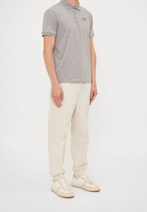 Szary polo z kołnierzykiem, w połączeniu z kremowymi spodniami typu tapered i jasnymi trampkami. Posiada małe haftowane logo.