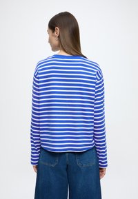 Tričko s dlhými rukávmi s modrými a bielymi vodorovnými pruhmi, z mäkkej látky, s okrúhlym výstrihom a voľným strihom, v kombinácii so širokými džínami s nohavicami do A.