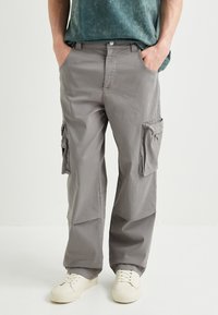 Pantaloni cargo grigi con multiple tasche, vestibilità comoda e una texture liscia. Le caratteristiche includono tasche laterali con cerniera e una vita sicura.
