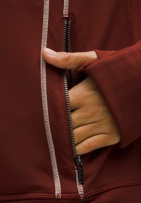 Giacca zip-up bordeaux con cuciture bianche a contrasto, dotata di tasca laterale, zip visibile e fori per il pollice sulle maniche.