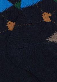 Calze navy realizzate in un materiale morbido, caratterizzate da un design di un pulcino marrone chiaro con un motivo a pois, su uno sfondo geometrico colorato.
