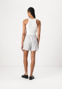 Hvit ribbestrikket tanktop kombinert med lette stripete shorts i blått og hvitt, med elastisk midje. Svart fottøy fullfører antrekket.