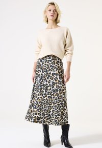 Pull beige avec un col large, associé à une jupe midi en imprimé léopard doré et noir. Des bottes à talons noires complètent la tenue.