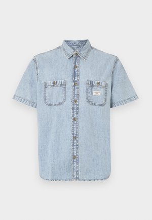 Chemise en denim bleu clair à manches courtes avec col pointu, deux poches poitrine et fermeture à boutons ; présente des détails cousus le long des coutures.