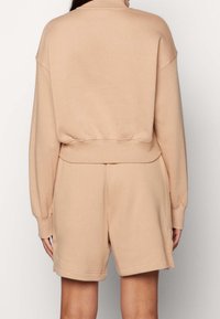 Light beige loungewear set featuring a cropped pullover with a high neck and elastic waist shorts, both made from soft, smooth fabric.