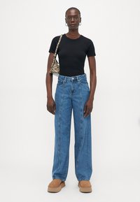 Svart topp med korte ermer, høytlivde lyseblå vide jeans, brune platå sko, og en svart-hvit stripete håndveske. Glatt tekstur.
