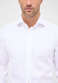 Witte dress shirt gemaakt van gladde stof met een klassieke kraag, lange mouwen en parelknopen in het midden. Gevarieerd oppervlakdetail.