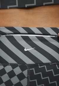 Czarno-szare odzież sportowa z geometricznymi wzorami, zamkiem błyskawicznym i białym logo Nike. Wykonana z teksturowanego, elastycznego materiału.