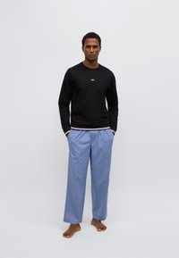 Juoda ilgomis rankovėmis džemperis su logotipu, derinamas su šviesiai mėlynomis laisvai krentančiomis kelnėmis. Kelnės turi elastingą juosmenį, be matomų raštų.