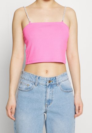 Top court côtelé rose avec des accents de fines bretelles torsadées. Associé à un jean en denim délavé clair doté d'une fermeture à bouton et de poches avant.