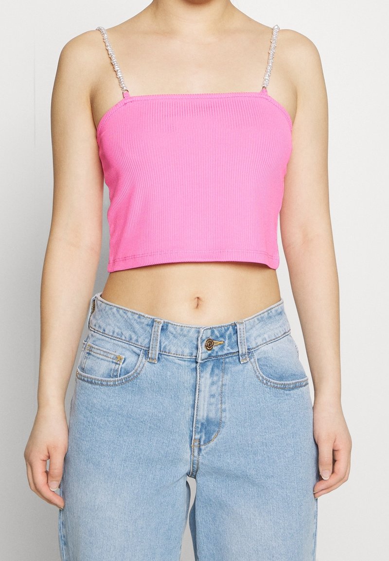 Różowy prążkowany top cropped z cienkimi, skręconymi paskami. Połączony z jasnoniebieskimi dżinsami z zapięciem na guzik i przednimi kieszeniami.