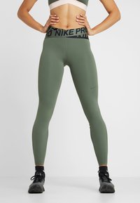 Groene legging gemaakt van rekbare stof, met een hoge tailleband met een zwart "NIKE PRO" logo en een kleine Nike swoosh op het bovenbeen.