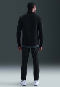 Svart langermet genser og svarte bukser med rett snitt, med et lagdelt utseende med en blå skjorte under og hvite sneakers.