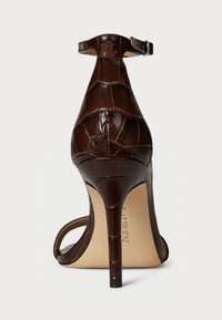 Sandalo alto marrone con texture in finta pelle di coccodrillo, cinturino alla caviglia regolabile e design a punta. Tacco a stiletto.
