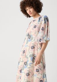 A floral dress in pastel colors features a flowing design with short flutter sleeves, made from lightweight fabric with black and blue floral accents.