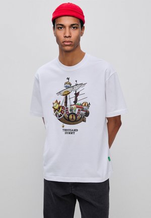 Young man wearing a red beanie and white T-shirt with a colorful cartoon pirate ship and the text "Thousand Sunny."