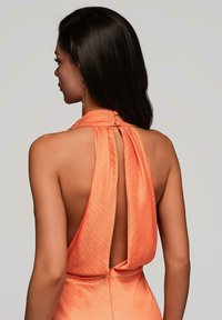 Vue arrière d'une robe sans manches orange avec un col montant, un dos décolleté et un accent bouton à la nuque, mettant en valeur un tissu doux et texturé.