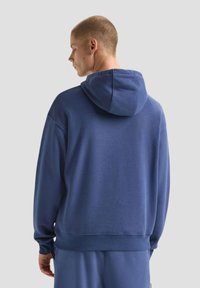 Felpa blu navy con una texture morbida, cappuccio regolabile e polsini a costine. Il design semplice presenta una vestibilità rilassata e minimi dettagli.