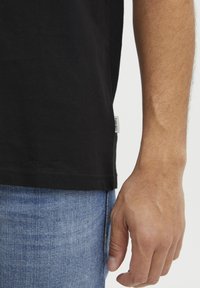 Fekete pamut póló, lekerekített nyakkal, rövid ujjakkal és oldalsó címkével, világoskék farmernadrággal párosítva.