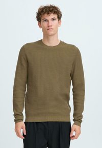 Pulover tricotat de culoare verde măsliniu, cu guler rotund, mâneci lungi și textură ribată. Are o cusătură ajustată la baza puloverului și la manșete.