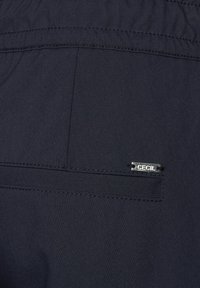 Marinblå tygbyxor med elastisk midja, med en bakficka och en silverfärgad "CECIL" logotypetikett. Slät textur och enkelt stygn.