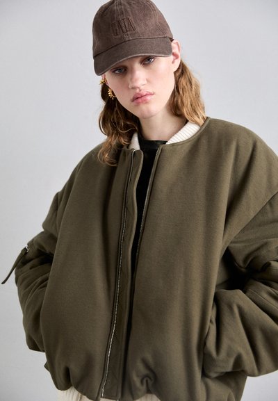 Giacca bomber oversize verde oliva con colletto bianco a coste e chiusura con zip, caratterizzata da maniche voluminose e tessuto testurizzato.