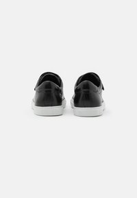 Baskets en cuir noir avec semelles en caoutchouc blanches. Présentent une finition lisse, un design arrondi et un style minimaliste sans logos ou accents visibles.