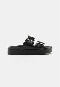 Sandalo platform nero con due fibbie regolabili color argento e suola spessa, mostrato di profilo su sfondo bianco.