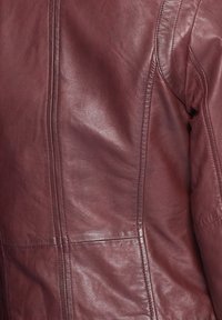 Acercamiento de una chaqueta de cuero burdeos que muestra el detallado del cosido y la textura en la parte de la espalda y el área de los hombros.