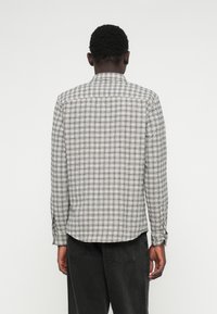 Juodai baltas patikrintas ilgomis rankovėmis marškinis. Yra klasikinis apykaklė, sagų rankogaliai ir išlenktas hem. Pagamintas iš lengvo audinio.